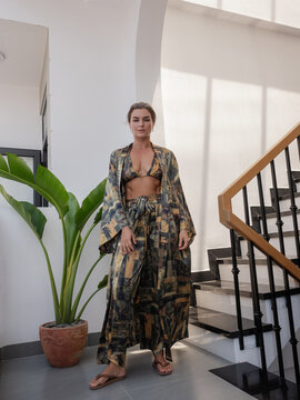 Woman modeling flowing patterned resort wear with bikini top and wide leg pants in bright modern interior