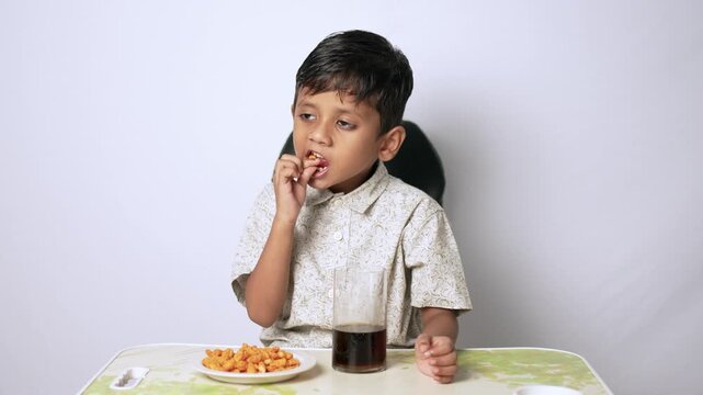 Indian boy eating snacks at home. Child enjoying unhealthy food and soda drink.