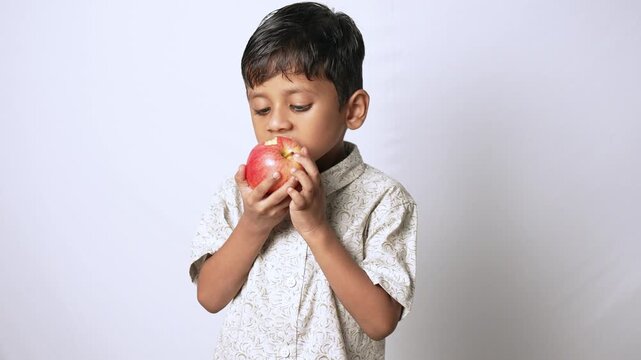 Indian boy eating a fresh red apple. Healthy child holding fruit for a nutritious snack.
