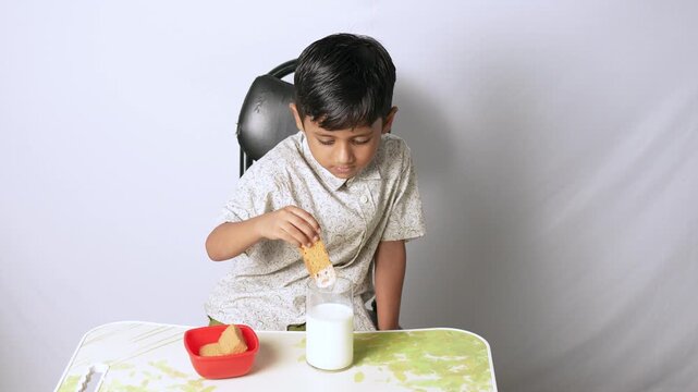 Indian boy dipping biscuit in milk. Child eating healthy snack at home in Delhi NCR.