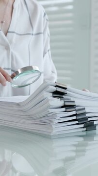 Woman's hands using a magnifying glass to scrutinize a document while holding a pen, researching important information for legal, financial, or academic analysis and validation