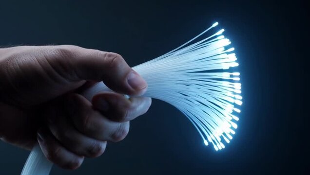 Hand holding a bundle of optical fiber strands, with the tips glowing brightly against a dark background.