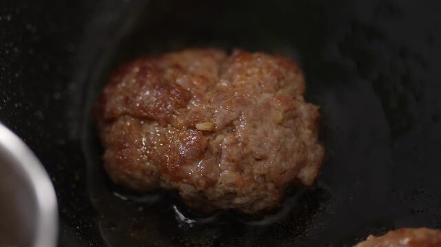 A juicy meat cutlet frying in a hot black pan.