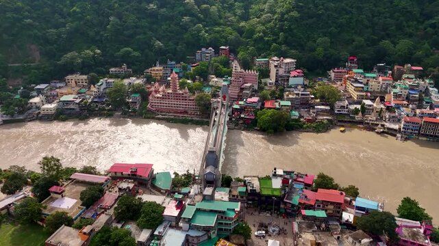 Aerial drone footage of Rishikesh during monsoon, showcasing the Ganges River, Ram Jhula, Lakshman Jhula, lush green Himalayan foothills, temples, and the scenic spiritual city of Uttarakhand.