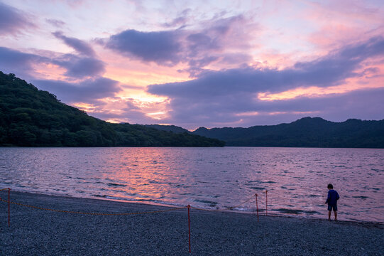 夕暮れの湖畔で幻想的な空を眺める子どもの後ろ姿
