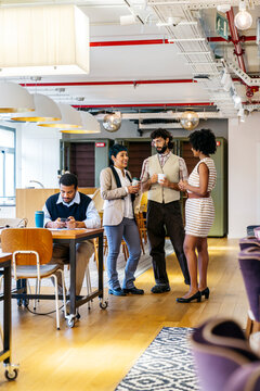 Diverse team of professionals networking and collaborating in a modern coworking office. One man working on his phone, others talking