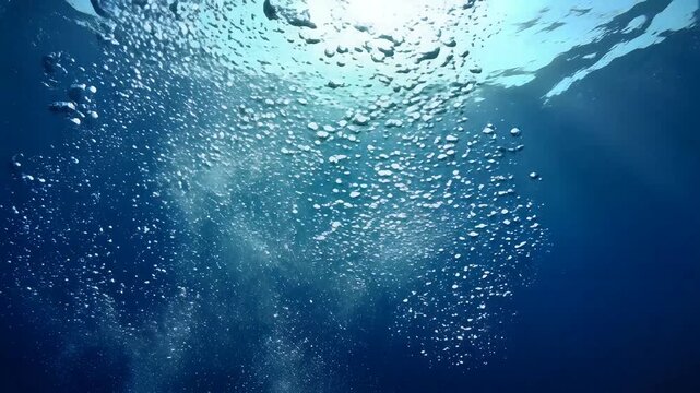 Underwater view of sunlight rays filtering through deep blue ocean water with rising air bubbles
