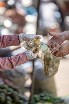 Purchasing goods for cash at local food market in Vietnam, seller giving charge to buyer with Vietnamese dong banknotes, vendor handling money to customer after purchase, money in exchange for goods.