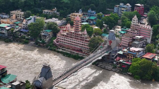 Aerial drone footage of Rishikesh during monsoon, showcasing the Ganges River, Ram Jhula, Lakshman Jhula, lush green Himalayan foothills, temples, and the scenic spiritual city of Uttarakhand.