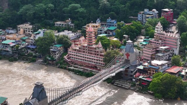 Aerial drone footage of Rishikesh during monsoon, showcasing the Ganges River, Ram Jhula, Lakshman Jhula, lush green Himalayan foothills, temples, and the scenic spiritual city of Uttarakhand.
