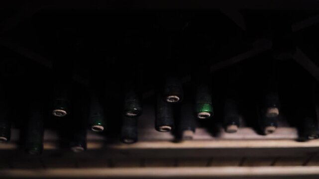 Old Dusty Wine Bottles Stored in Historic Wine Cellar, Vintage Glass Bottles Resting on Wooden Racks During Wine Aging Process, Traditional Winery Storage with Atmospheric Lighting, Alcohol Collection