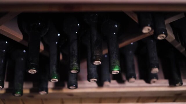 Old Dusty Wine Bottles Stored in Historic Wine Cellar, Vintage Glass Bottles Resting on Wooden Racks During Wine Aging Process, Traditional Winery Storage with Atmospheric Lighting, Alcohol Collection