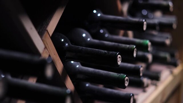 Old Dusty Wine Bottles Stored in Historic Wine Cellar, Vintage Glass Bottles Resting on Wooden Racks During Wine Aging Process, Traditional Winery Storage with Atmospheric Lighting, Alcohol Collection