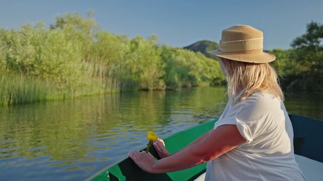 Woman enjoying a peaceful boat ride through the tranquil wetlands of Skadar Lake in Montenegro while holding a yellow water lily
