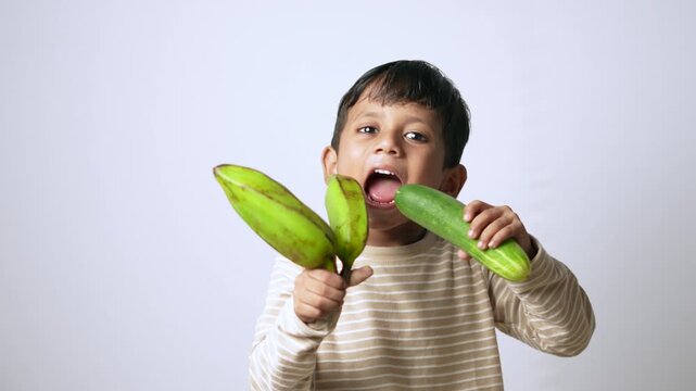 Indian boy holding fresh vegetables. Child eating healthy green produce for nutrition.