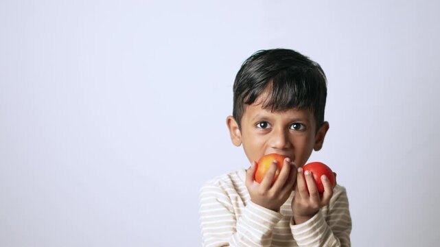 Indian boy eating fresh tomato. Healthy child enjoying organic vegetable snack.