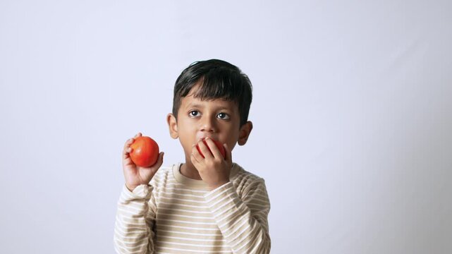 Indian boy eating fresh tomato. Healthy child holding organic vegetables for nutrition.