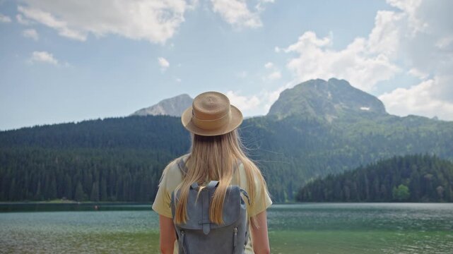 Young woman with backpack enjoying the view of Black Lake in Durmitor National Park, Montenegro. Mountain landscape with crystal clear water