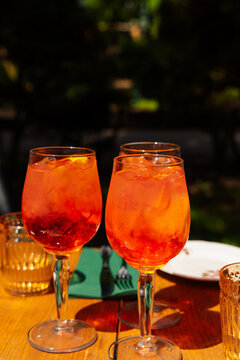 Friends enjoy Aperol cocktail at a sunny outdoor table during a summer afternoon gathering in the park