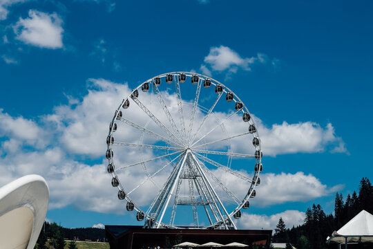 Ferris wheel stands tall against blue sky with clouds in mountain area