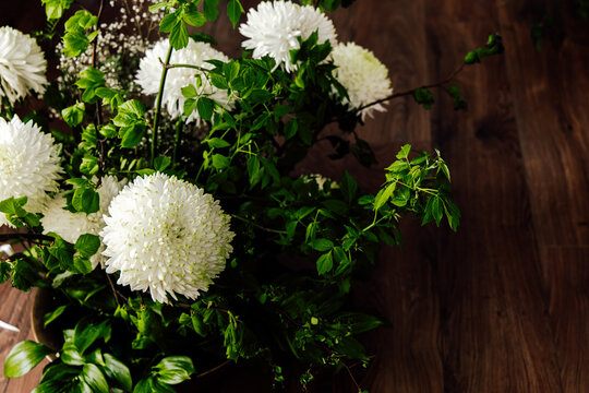 White chrysanthemum flowers arranged with green leaves on wooden surface at indoor location in the afternoon