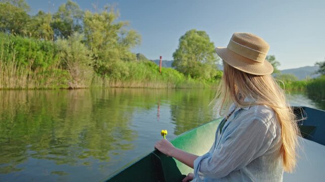 Woman holding a yellow water lily while enjoying a peaceful boat ride through the waterways of Skadar Lake in Montenegro.
