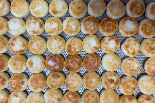 Semi-finished cottage cheese pancakes Syrnyky arranged on a tray in a food production facility during daytime