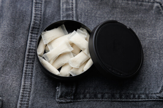 Snus pouches in a black container on denim fabric at a casual setting during daylight