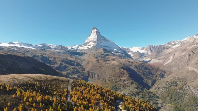 Aerial drone view of the Matterhorn mountain peak rising above a colorful autumn forest in Switzerland on a bright sunny day. Alpine autumn landscape.