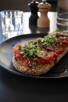 Bruschetta gourmet al pomodoro fresco con acciughe e microortaggi servita su un piatto nero in un ristorante moderno