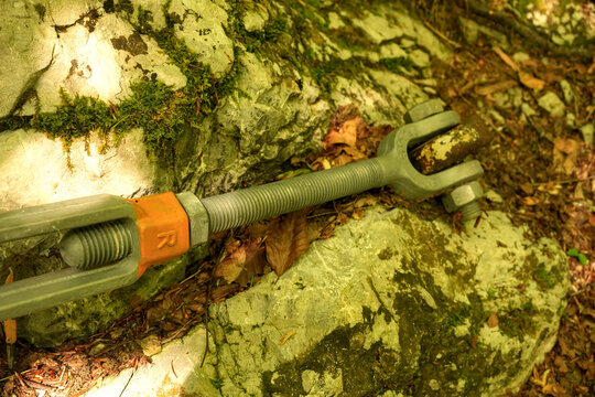 Heavy-duty steel turnbuckle and threaded tension rod anchored to a rock surface. Industrial hardware and structural bridge engineering detail.