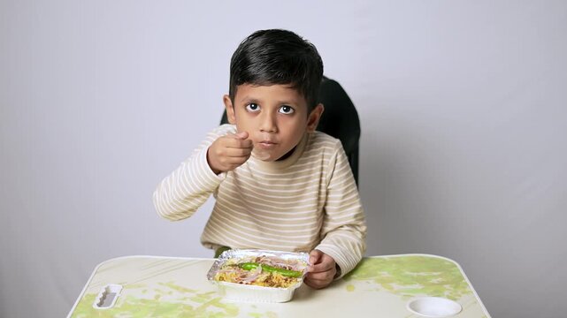 Indian boy eating food from container. Cute child having lunch at home.