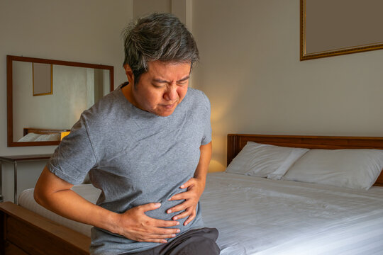 Person holding stomach in pain, illustrating abdominal disorders and medical treatment concept in home setting.