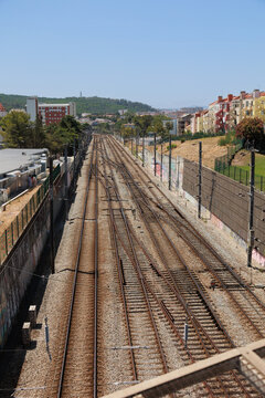 Multiple railway tracks running through an urban corridor in Lisbon, Portugal. Captured from an elevated viewpoint, the image highlights railway infrastructure, parallel train lines