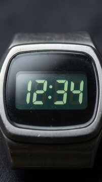 Close-up of a retro digital wristwatch featuring a green display showing 12:34 set within a brushed metal case