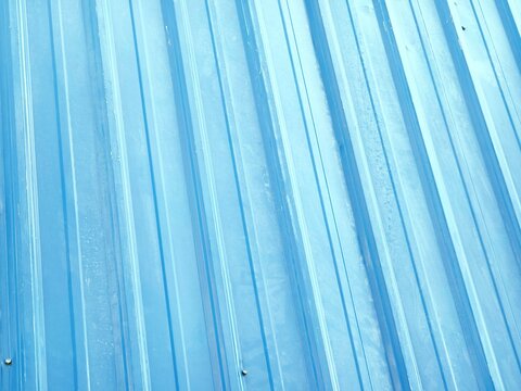 High-angle close-up shot of a bright blue corrugated metal roofing sheet showing vertical parallel lines, textured surface, and weathered industrial steel pattern.
