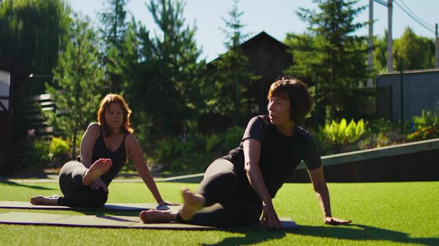 Elderly women practicing slow motion Pilates together on outdoor grass mats, focusing on gentle core strength, balance, and mindful senior fitness exercise