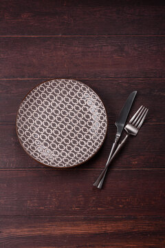 An empty round ceramic plate on a dark, textured brown background. An empty round plate