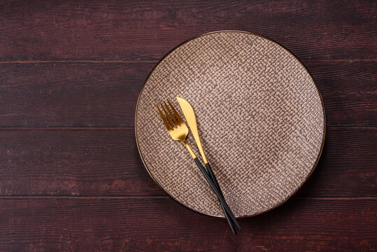 An empty round ceramic plate on a dark, textured brown background. An empty round plate