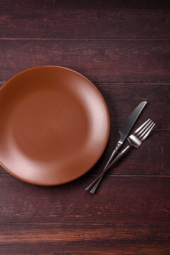 An empty round ceramic plate on a dark, textured brown background. An empty round plate