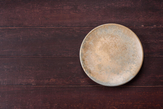 An empty round ceramic plate on a dark, textured brown background. An empty round plate