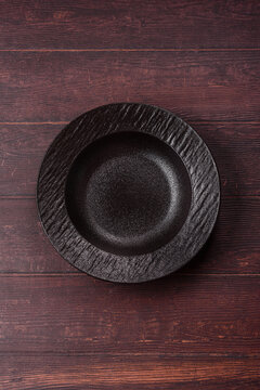An empty round ceramic plate on a dark, textured brown background. An empty round plate