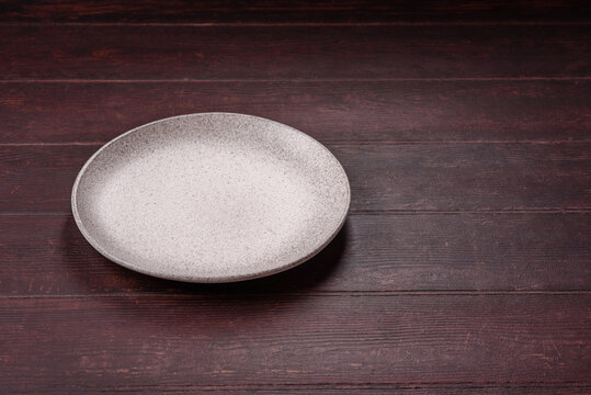 An empty round ceramic plate on a dark, textured brown background. An empty round plate