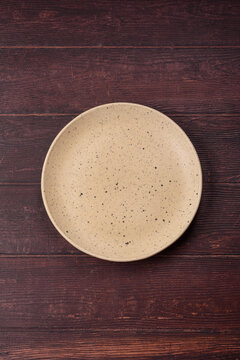 An empty round ceramic plate on a dark, textured brown background. An empty round plate