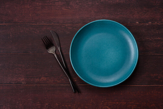 An empty round ceramic plate on a dark, textured brown background. An empty round plate