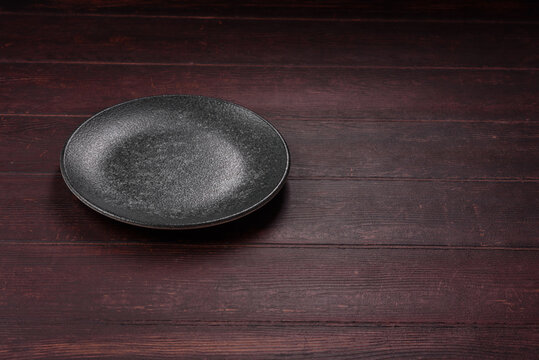An empty round ceramic plate on a dark, textured brown background. An empty round plate