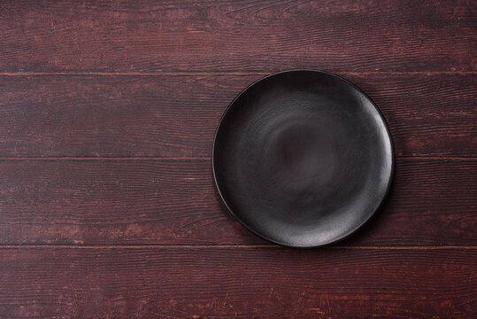 An empty round ceramic plate on a dark, textured brown background. An empty round plate