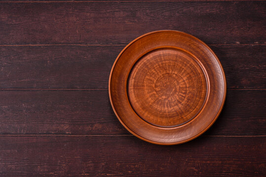 An empty round ceramic plate on a dark, textured brown background. An empty round plate
