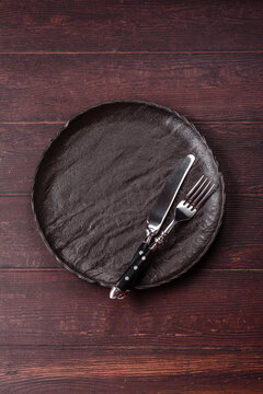 An empty round ceramic plate on a dark, textured brown background. An empty round plate