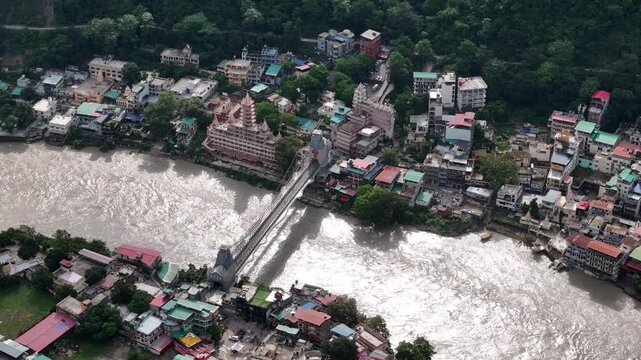 Aerial drone footage of Rishikesh during monsoon, showcasing the Ganges River, Ram Jhula, Lakshman Jhula, lush green Himalayan foothills, temples, and the scenic spiritual city of Uttarakhand.